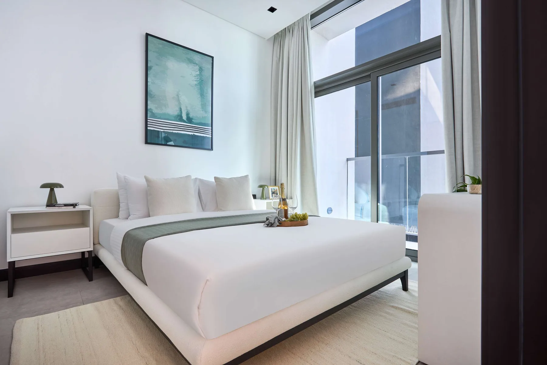 Un dormitorio luminoso con una cama tendida junto a ventanas altas y cortinas.