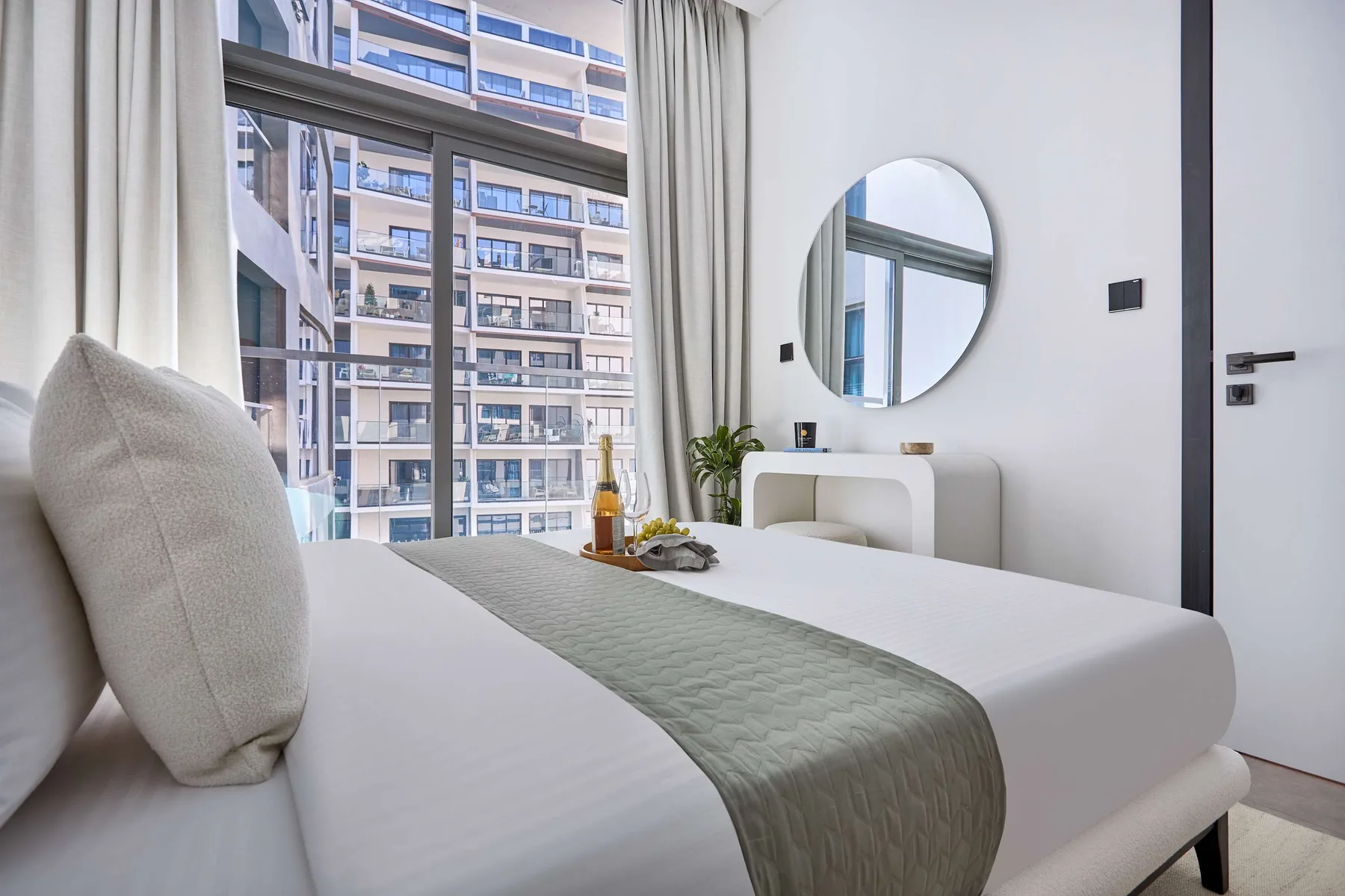 Un dormitorio luminoso con una cama tendida y un espejo redondo en la pared.
