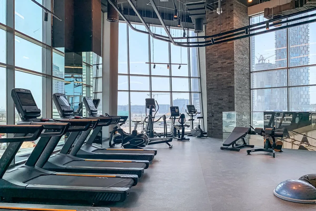 Un gimnasio con máquinas de cardio y equipo de ejercicio junto a grandes ventanales.