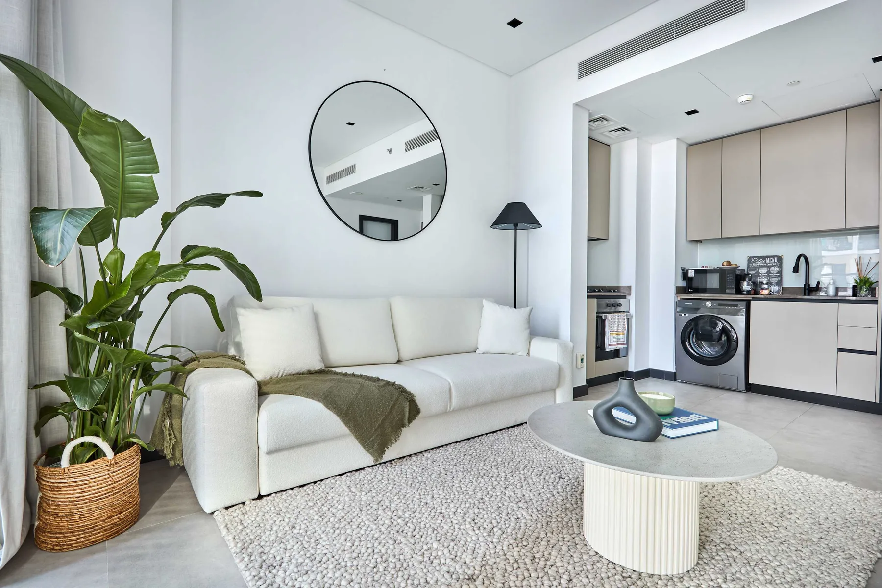 A bright living area with white seating, a round coffee table, and a potted plant.