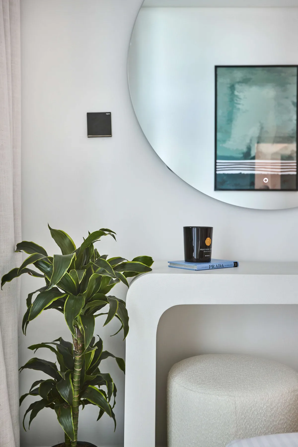 Un rincón luminoso de dormitorio con una planta frondosa junto a un cabecero curvo tapizado.