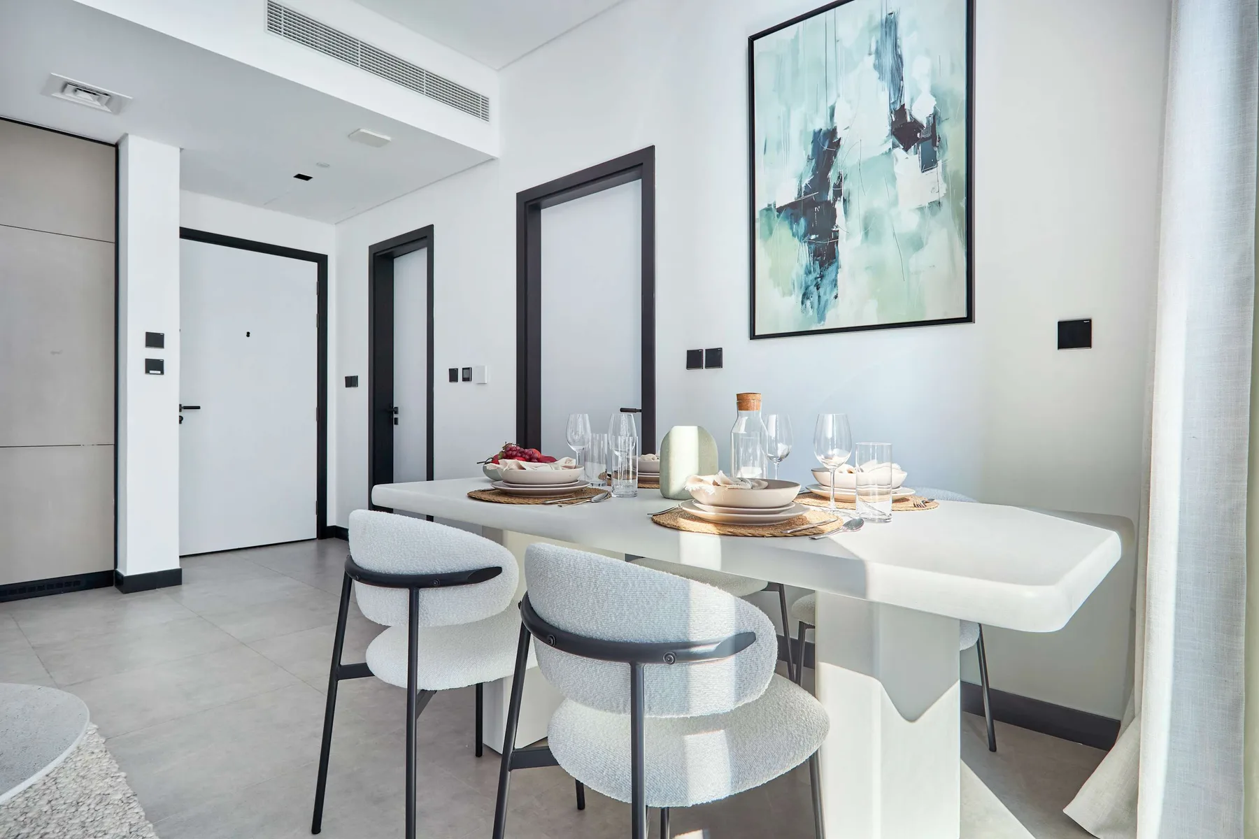 Un comedor luminoso con una mesa blanca puesta bajo una pintura abstracta.