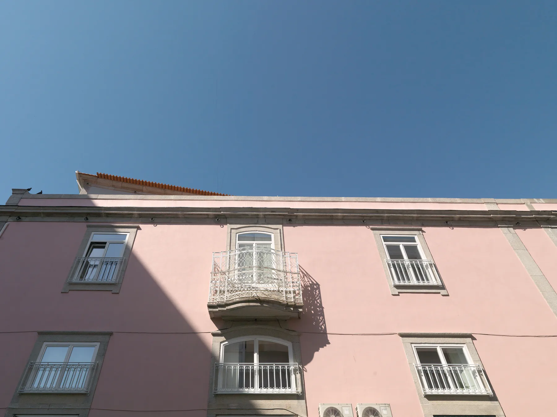 Fachada de un edificio rosa con balcones y ventanas bajo un cielo azul despejado.