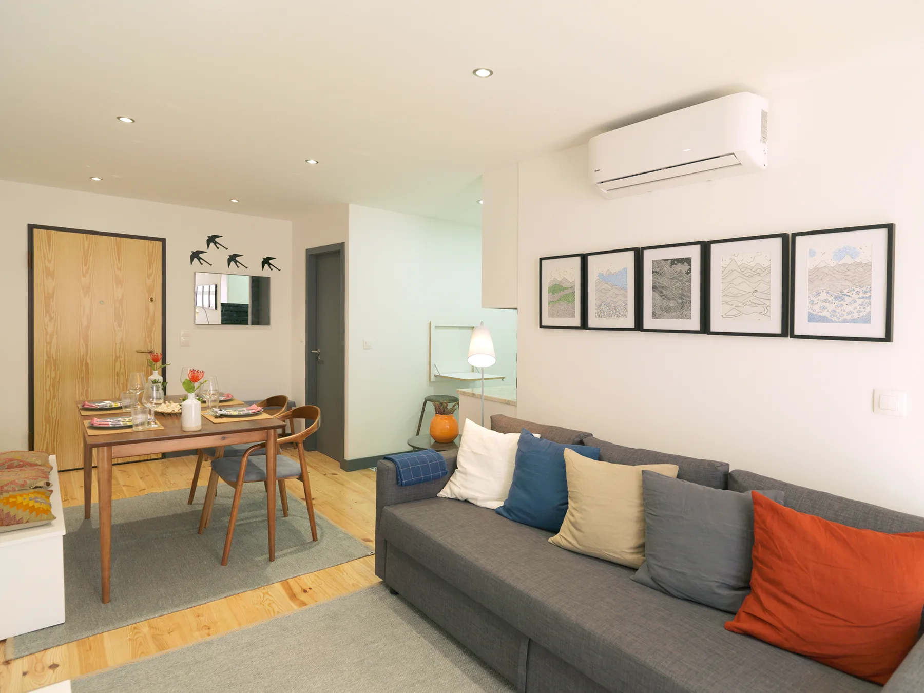 Sala de estar con un sofá gris, cuadros enmarcados y un comedor.