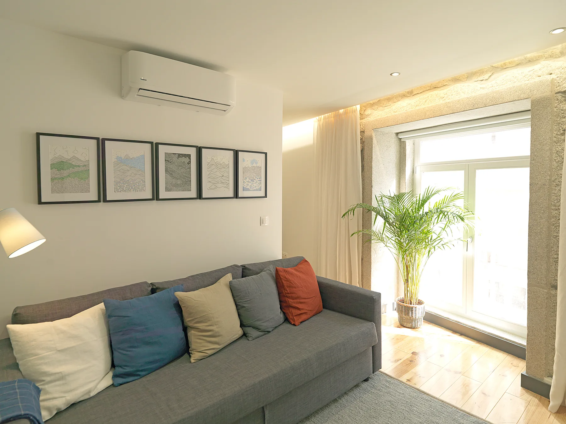 Una sala de estar con un sofá gris, cuadros enmarcados y una ventana luminosa.