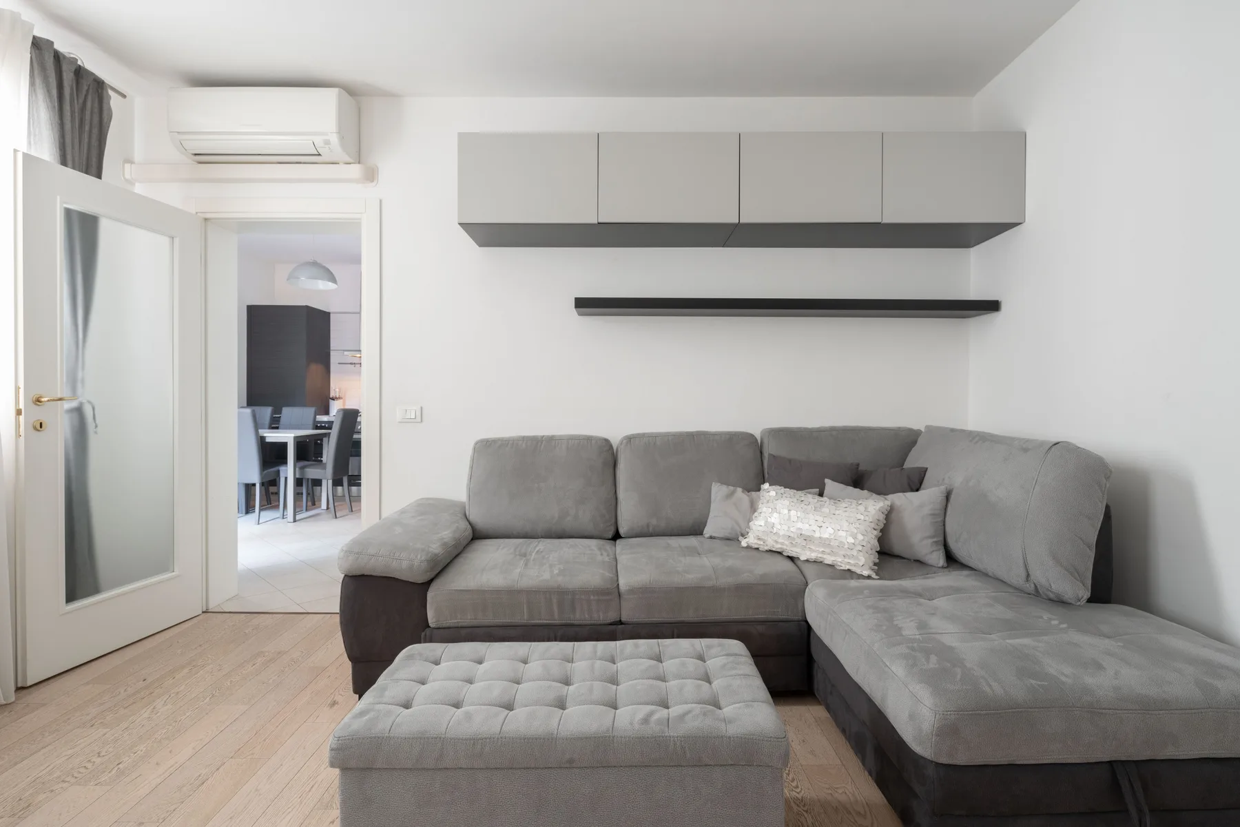 A living room with gray seating, a matching ottoman, and wall-mounted cabinets.