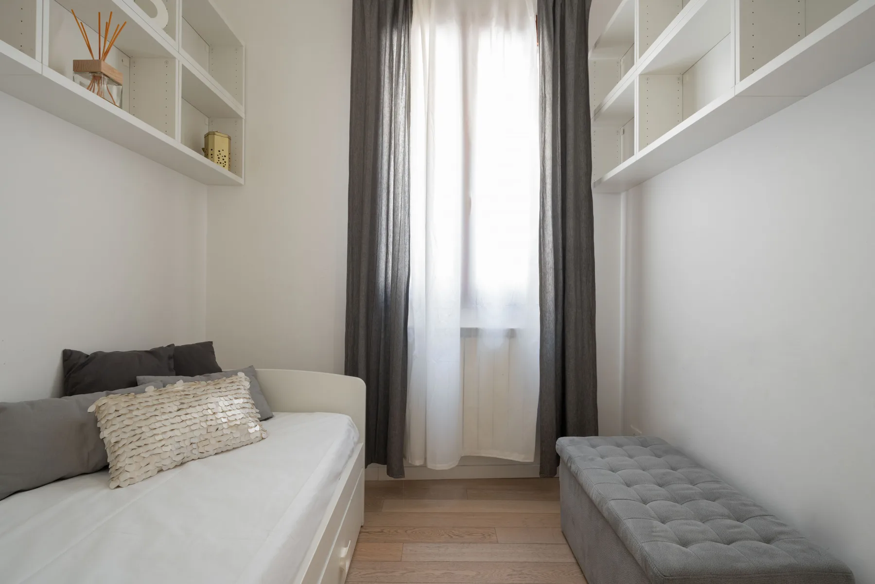 A small bedroom with a bed, a cushioned bench, and a curtained window.