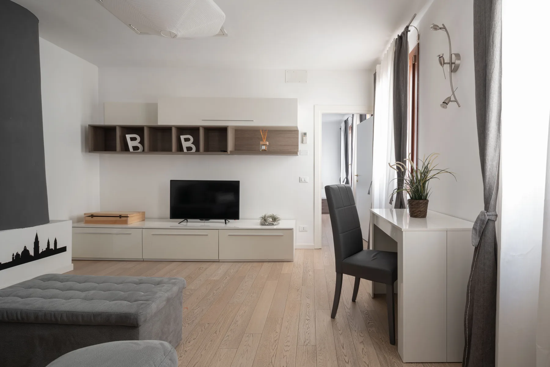 A bright living and dining area with a television, seating, and a desk by the window.