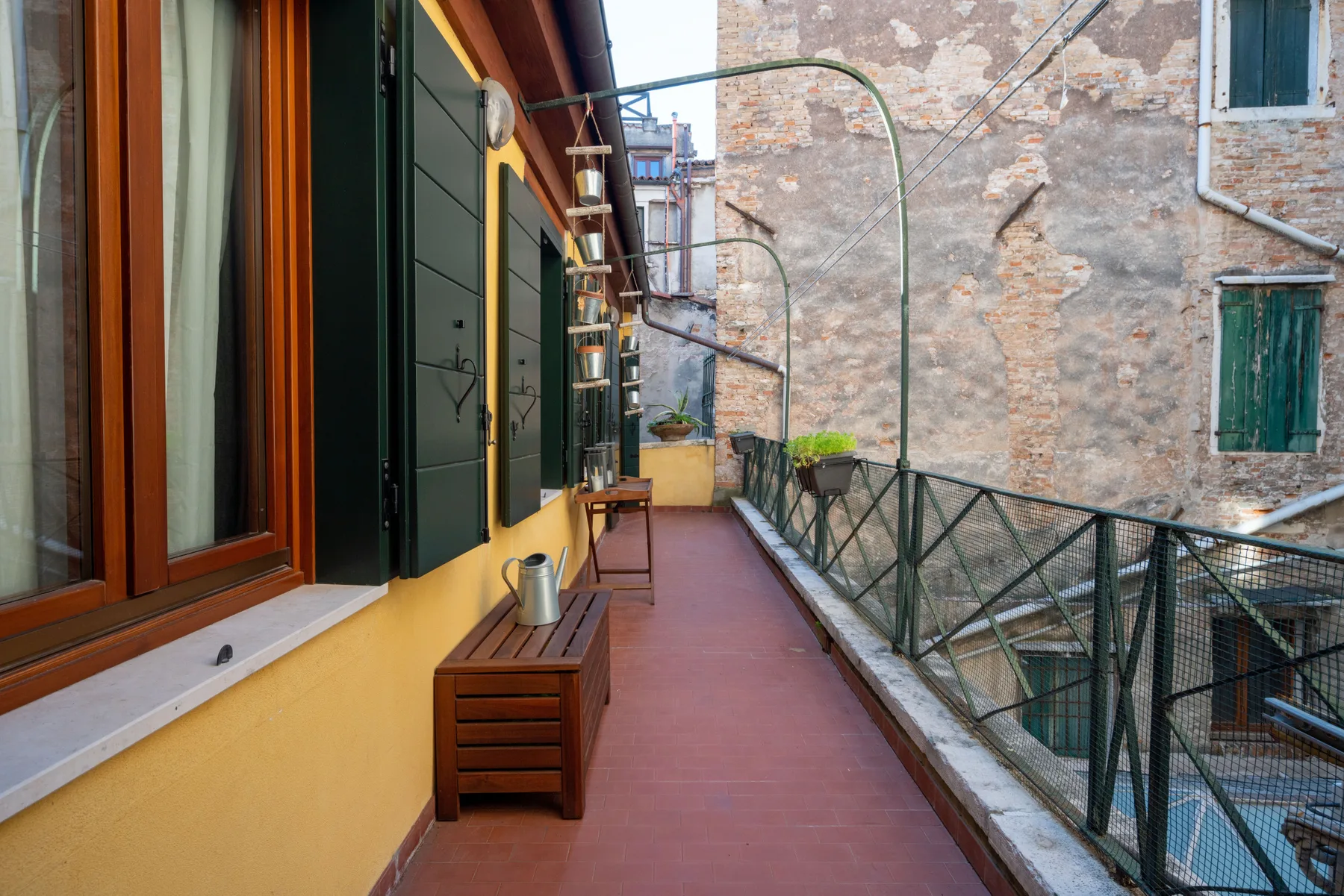 A narrow outdoor terrace runs beside a yellow building, with a metal railing.