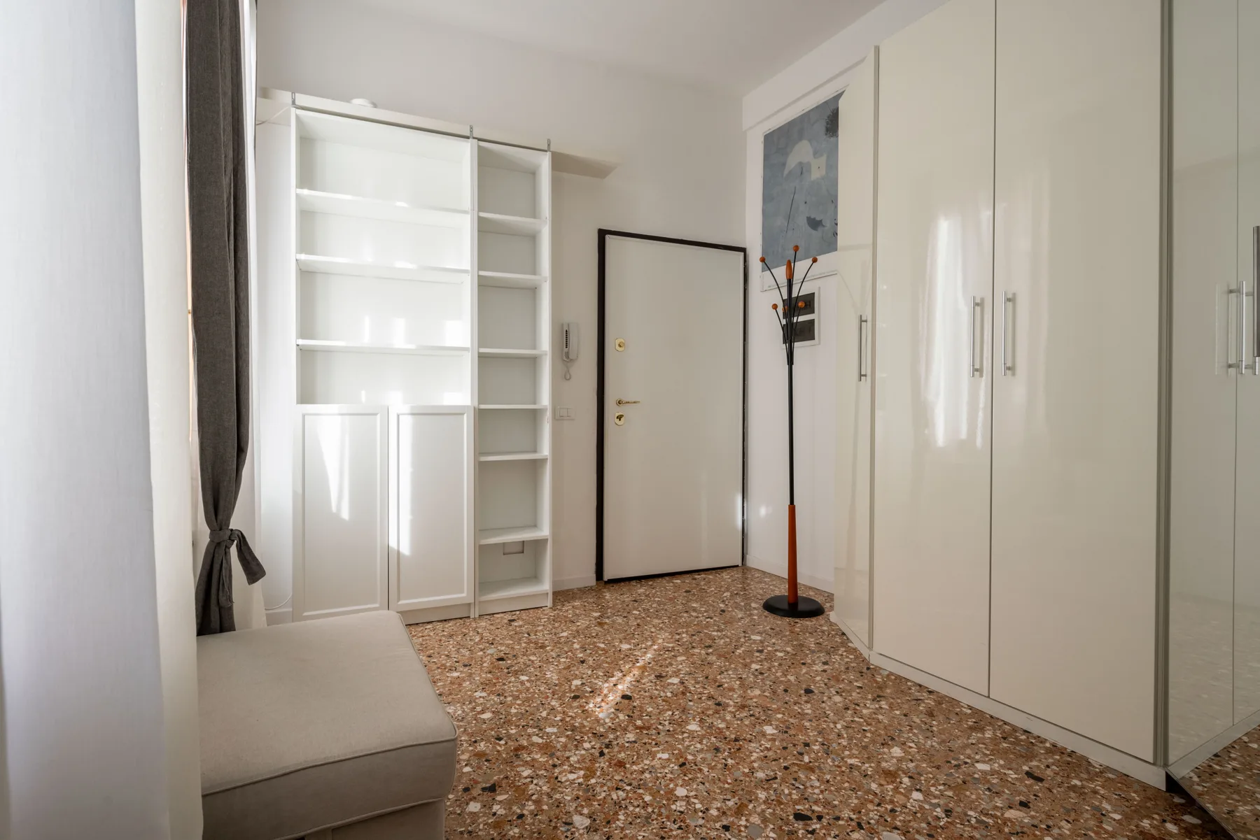A bright entryway with built-in shelving, wardrobes, and a closed door.