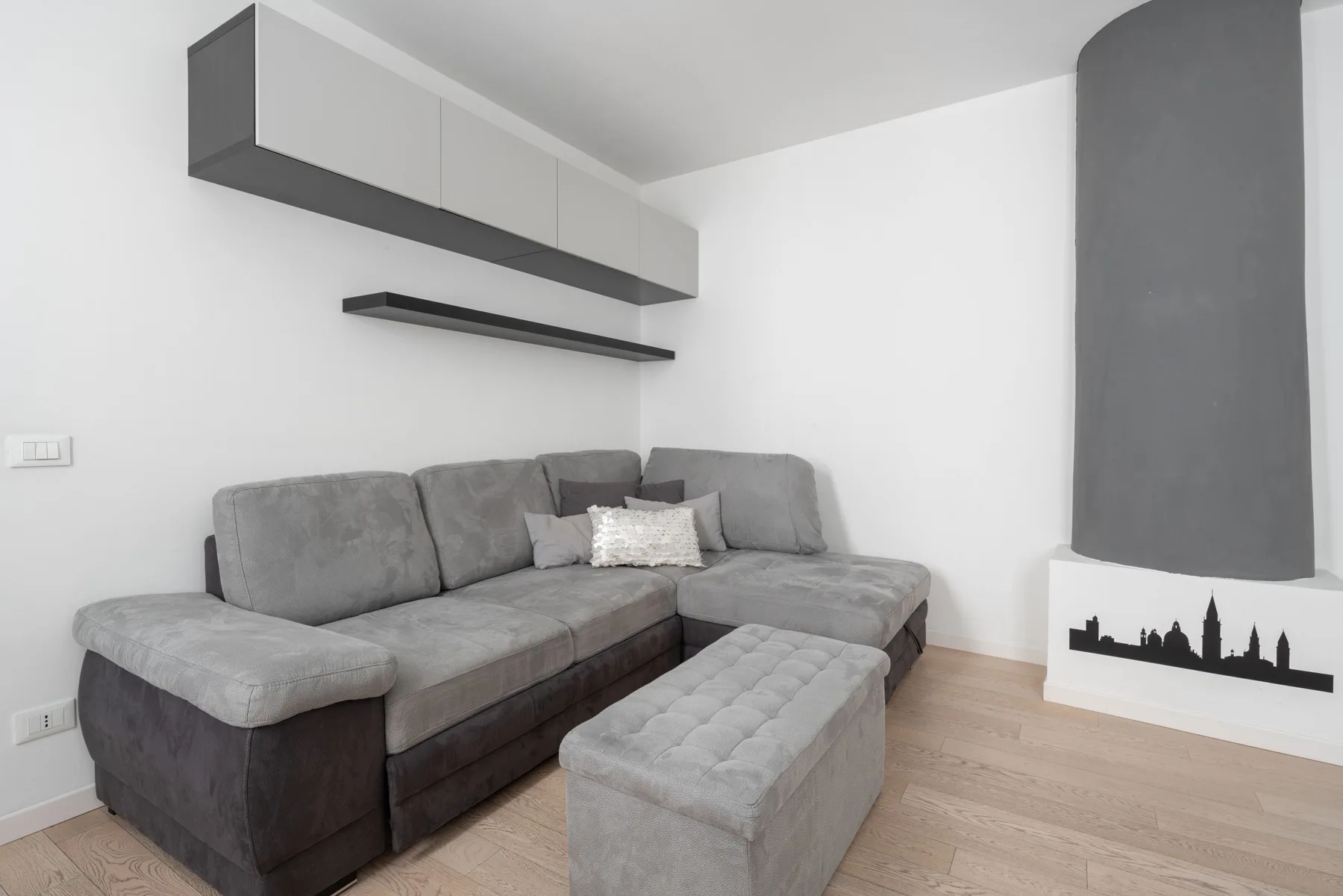 A living room with gray sectional seating and a matching upholstered ottoman.