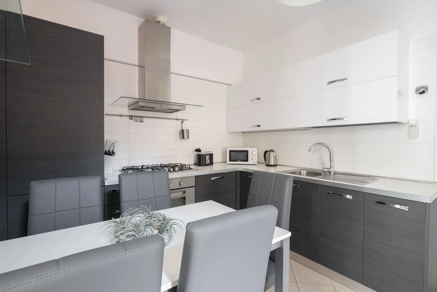 A modern kitchen with dark cabinets, white countertops, and a dining table.
