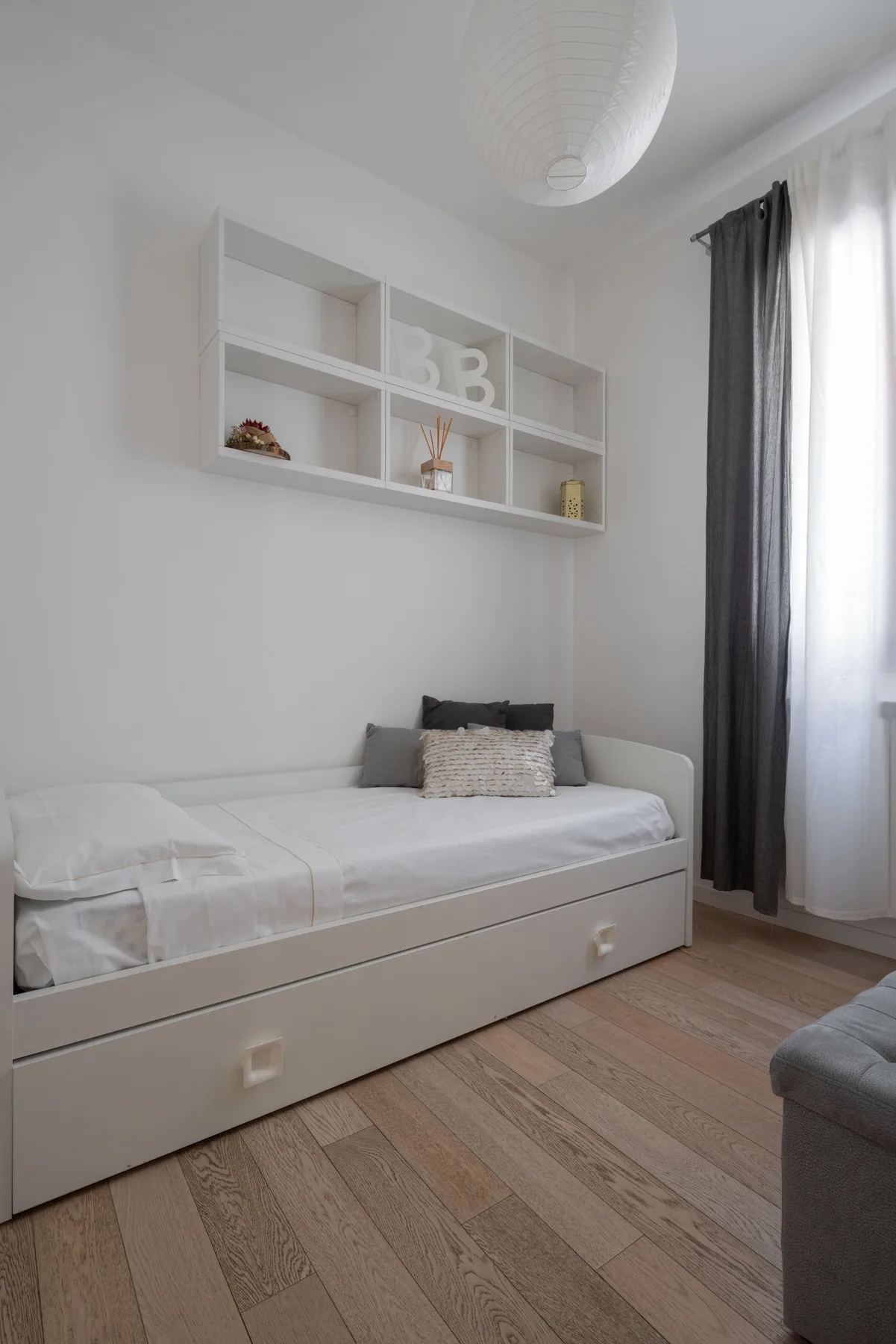 A bright bedroom with a white daybed beneath wall-mounted shelves.