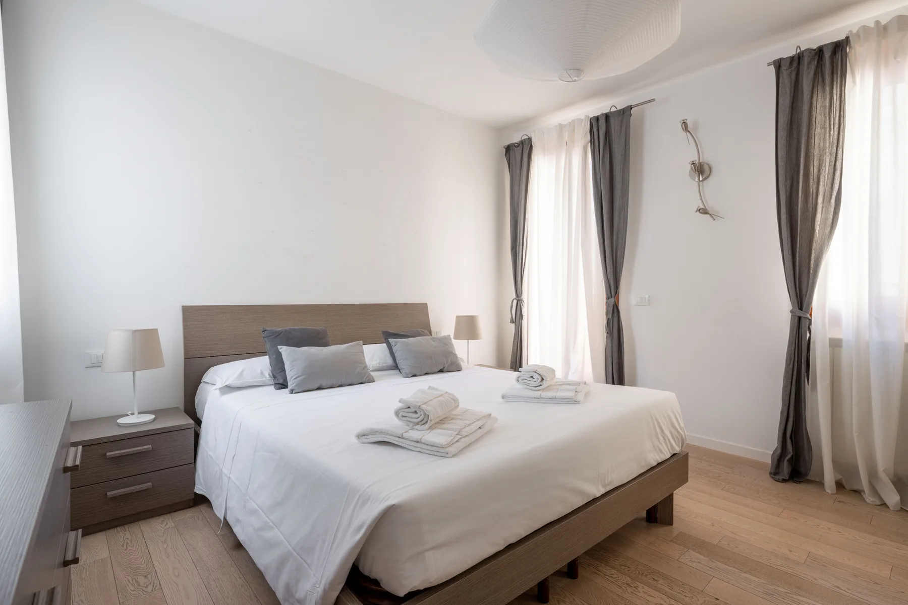 A bright bedroom with a large bed and tall curtained windows.