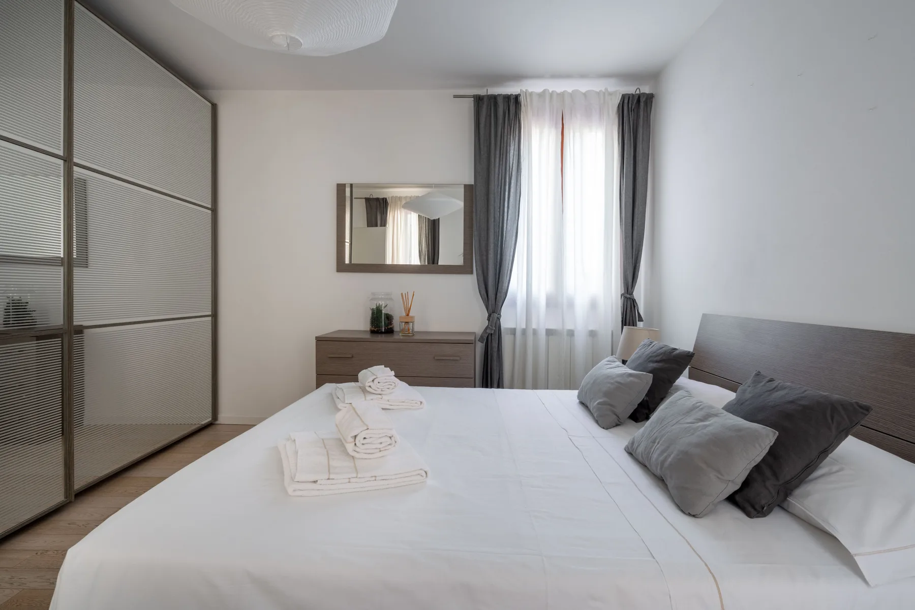 A bedroom with a neatly made bed and a curtained window.