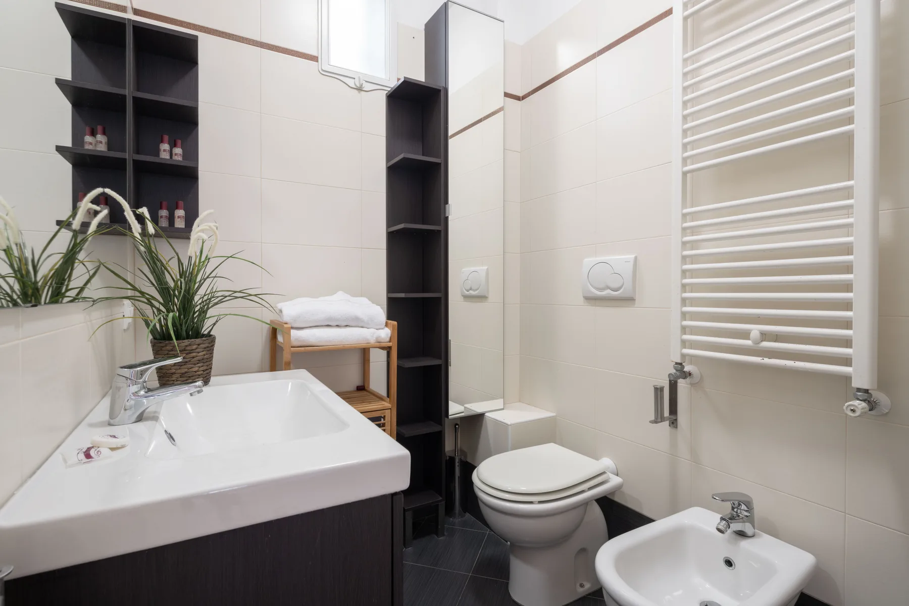 A tiled bathroom with a sink, toilet, and wall-mounted towel warmer.