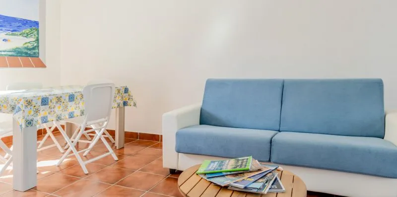 A living area with blue seating, a small table, and a dining table.