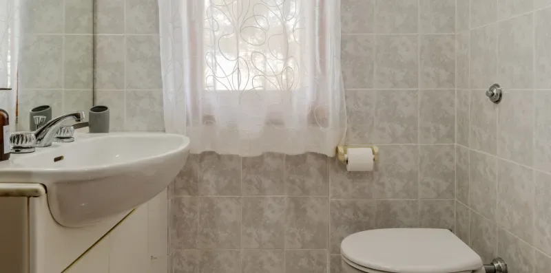 A tiled bathroom with a sink, toilet, and window.