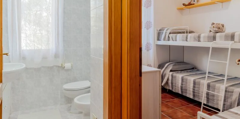 A bathroom with a window is visible beside a bedroom with bunk beds.