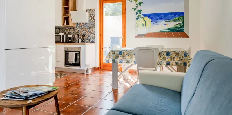 A bright living area with a blue seating area, a table, and a compact kitchen.