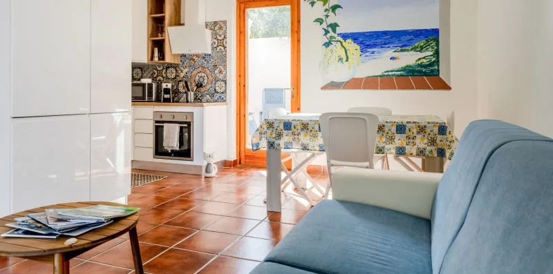 A bright kitchen and dining area opens into a living space with blue seating.