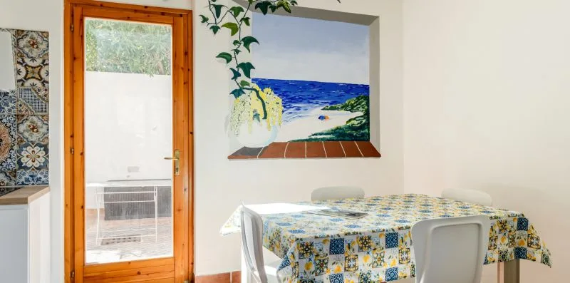 A dining area with a table covered by a patterned cloth and a beach painting on the wall.