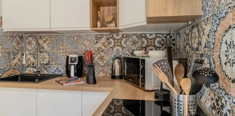 A kitchen counter with a sink, small appliances, and utensils against patterned tile.