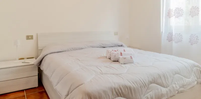 A bedroom with a neatly made bed beside a curtained window.