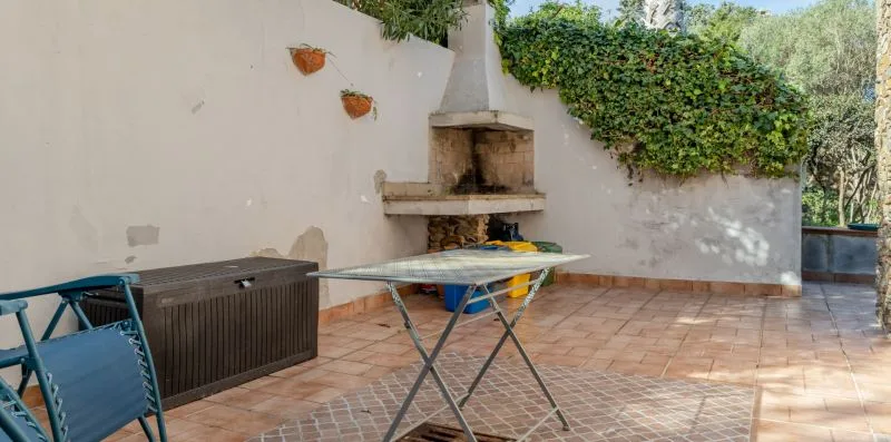 A tiled outdoor patio with a table, chairs, and a built-in barbecue.