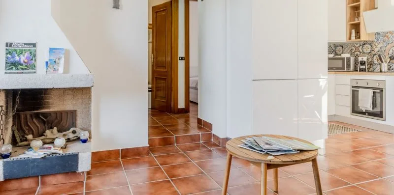 A tiled living area with a fireplace, a small table, and an adjoining kitchen.