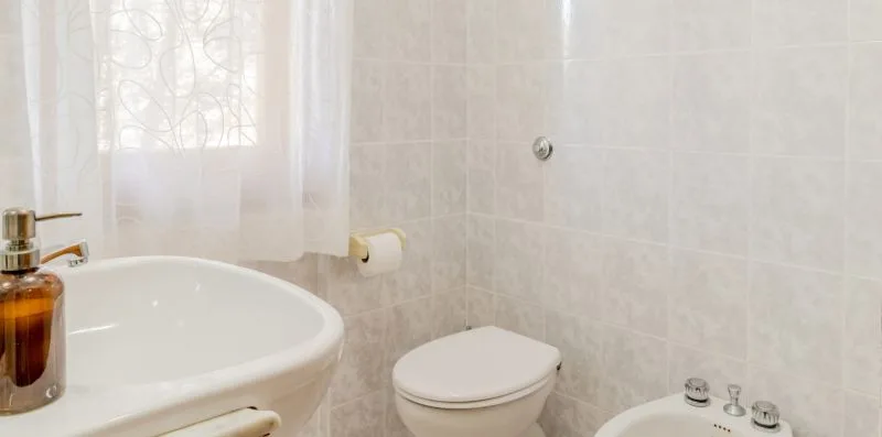 A tiled bathroom with a sink, toilet, and window.
