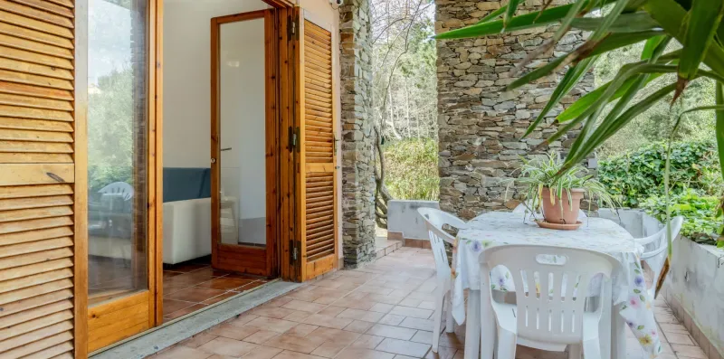 A tiled patio with a white table and chairs beside wooden doors and stone walls.