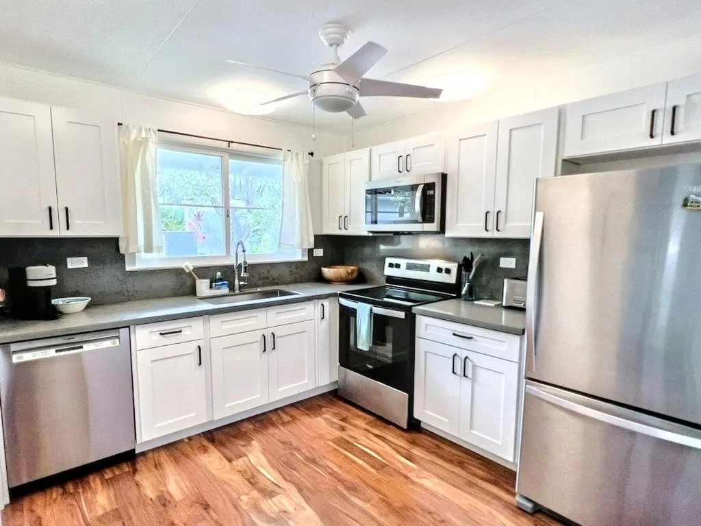A bright kitchen with white cabinetry, dark countertops, and stainless steel appliances.