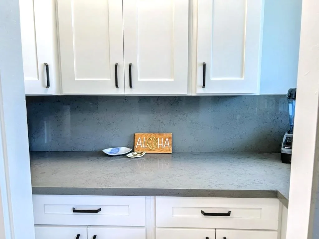 A kitchen counter with white cabinets and a gray backsplash.