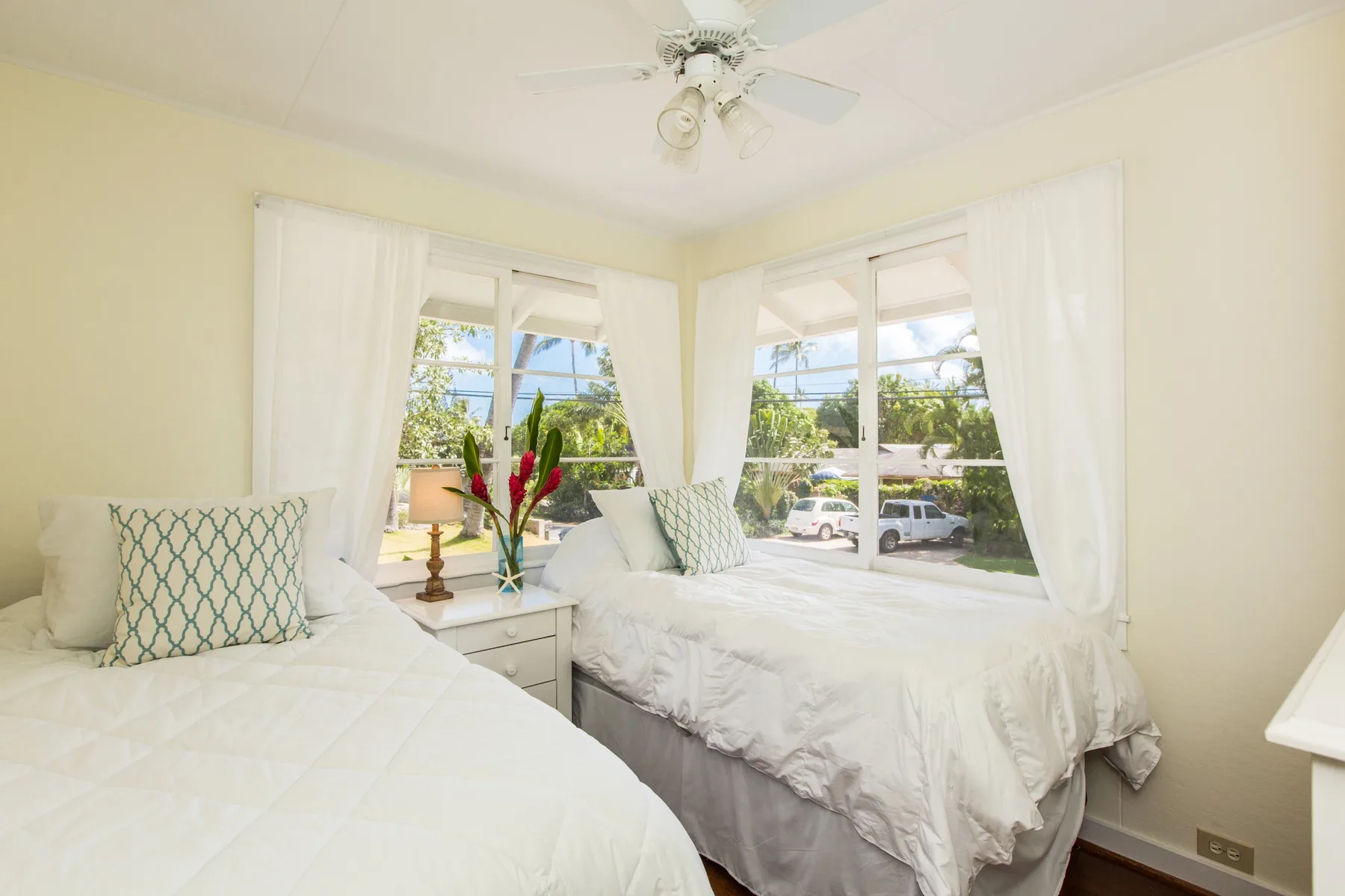 A bright bedroom with two beds beside large curtained windows.