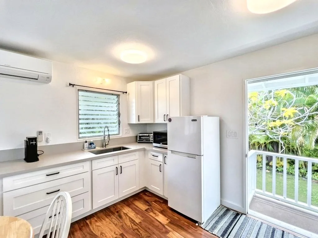 A bright kitchen with white cabinets, a refrigerator, and a sliding glass door.