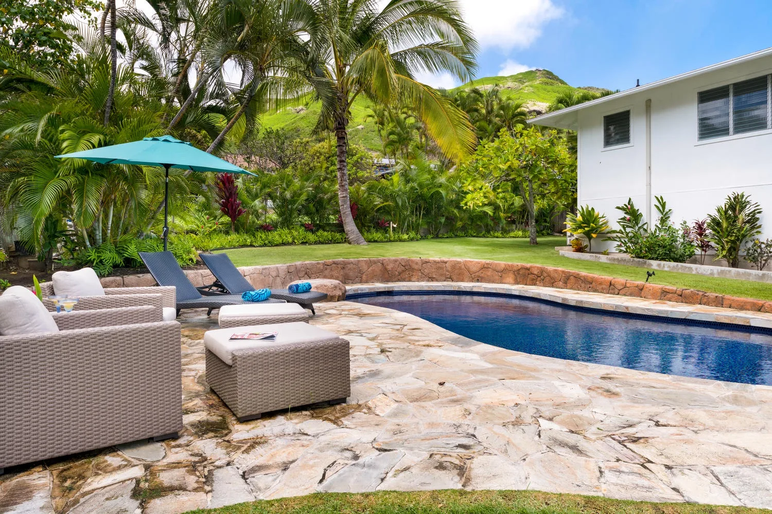 A poolside patio with outdoor seating, an umbrella, and tropical greenery.