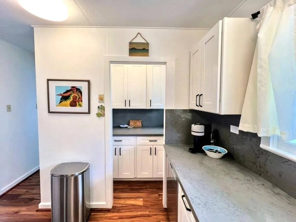 A compact kitchen with white cabinets, a long counter, and a curtained window.