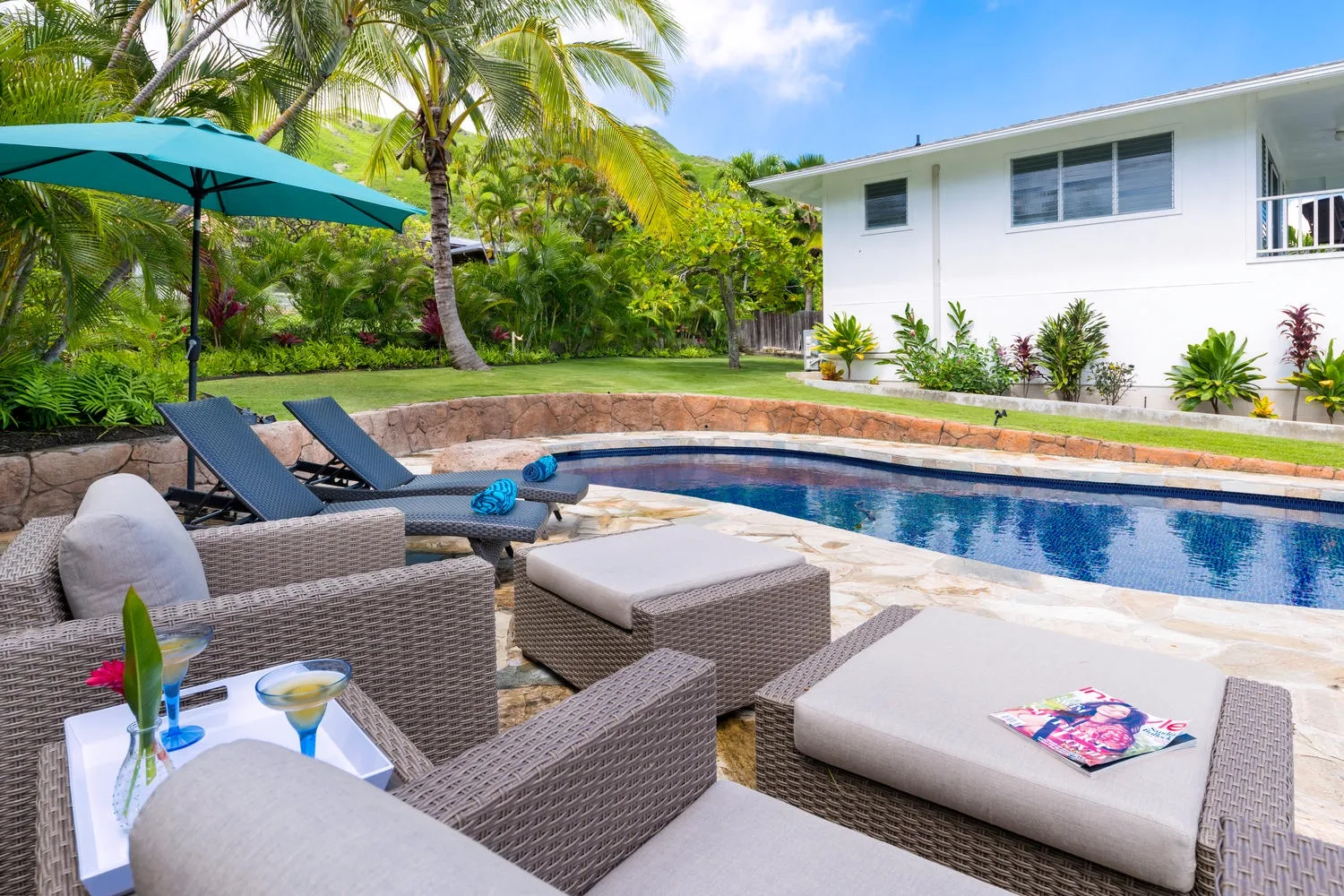 A swimming pool beside an outdoor seating area and a white building.