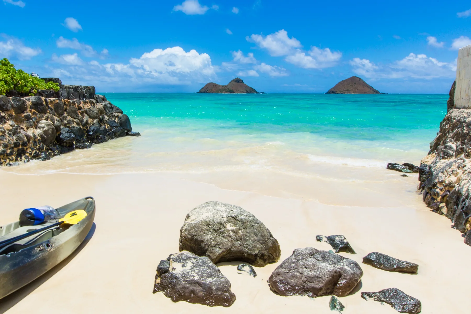 A sandy beach meets turquoise water, with a kayak and rocks along the shore.