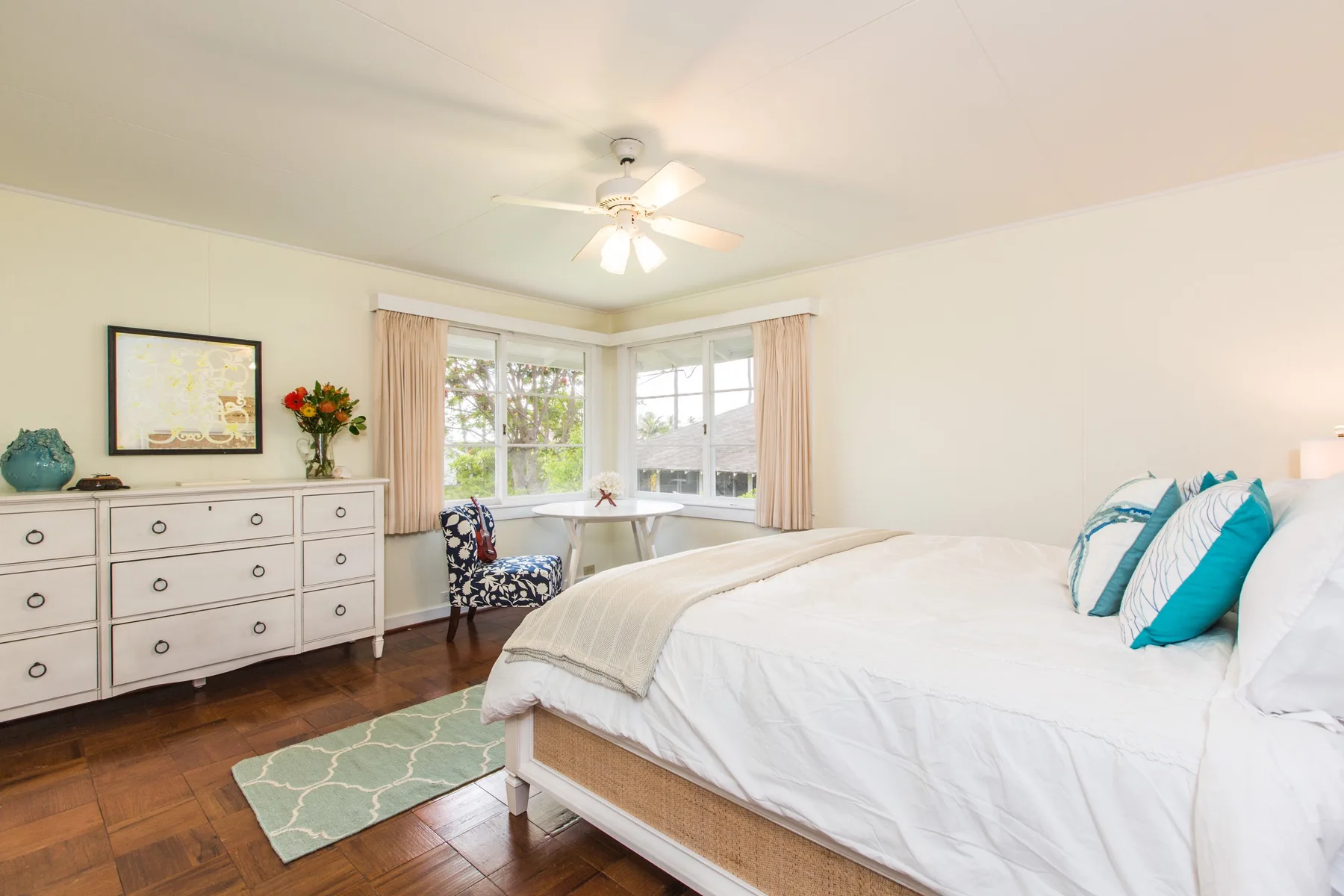 A bright bedroom with a bed beside large corner windows.