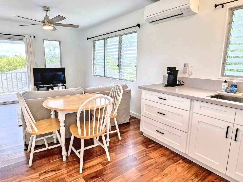 A bright dining and living area with a wooden table beside a white kitchen counter.
