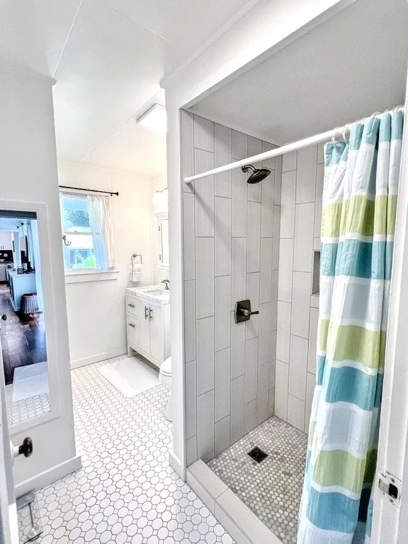 A bright bathroom with a tiled shower and a striped curtain.
