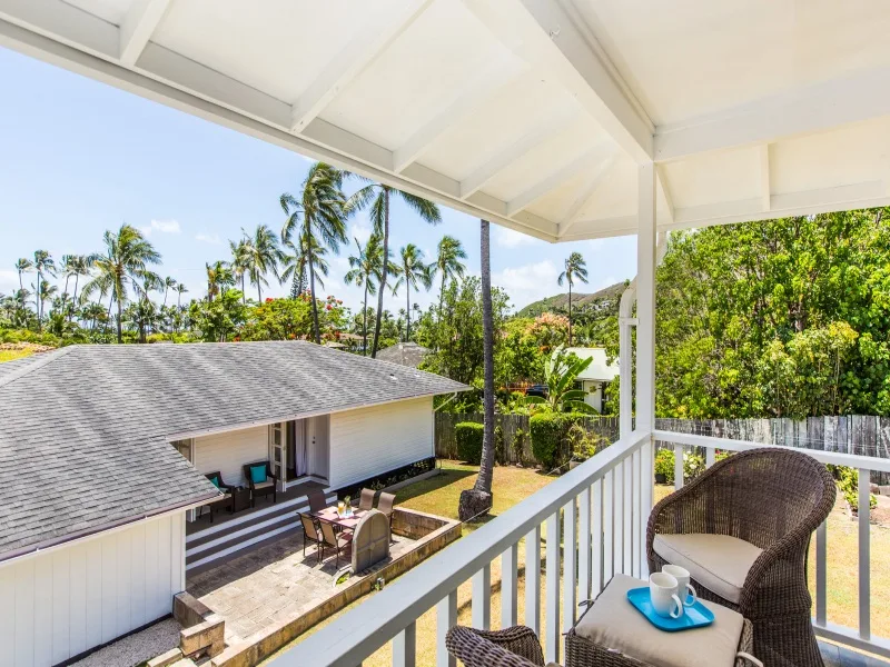 A covered balcony overlooks a house and tropical greenery.