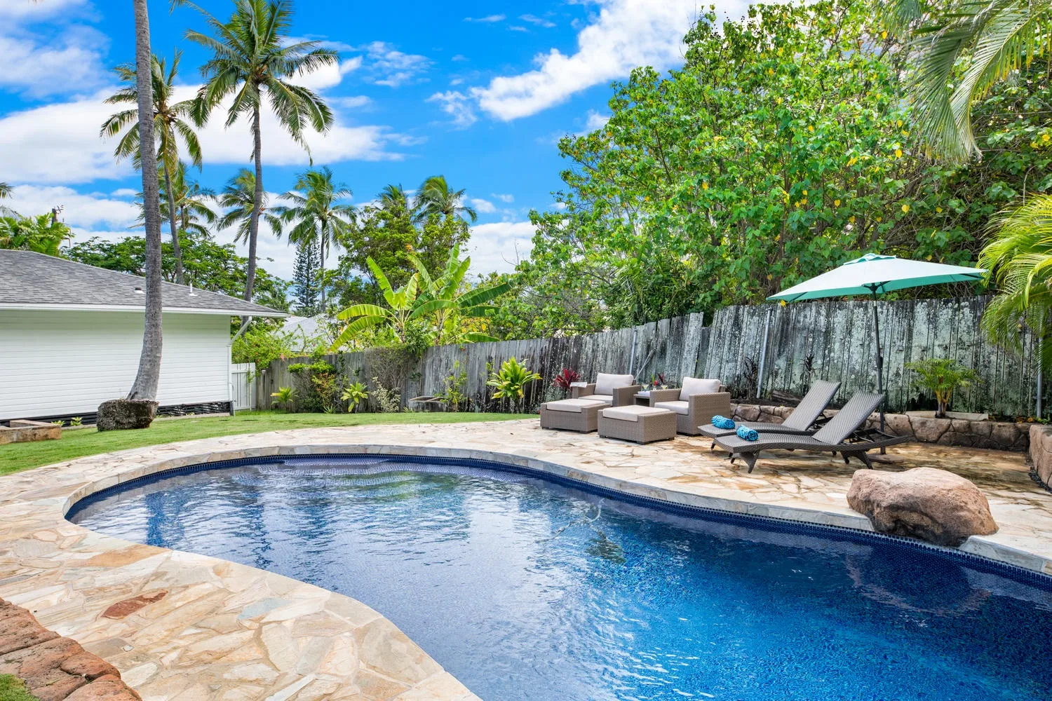 An outdoor swimming pool is surrounded by stone paving and lounge seating.
