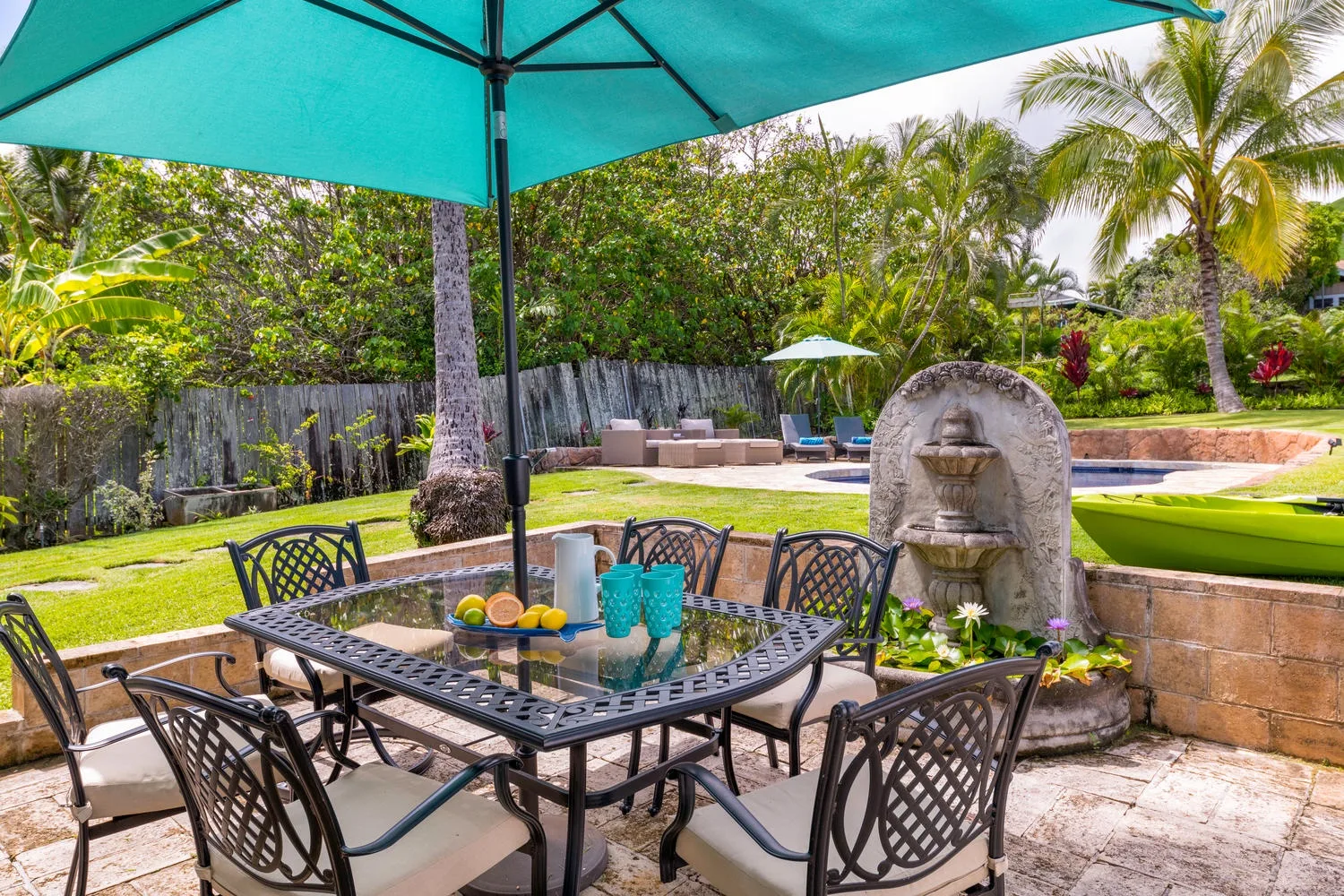 Una zona de comedor al aire libre con mesa y sillas junto a una piscina ajardinada.