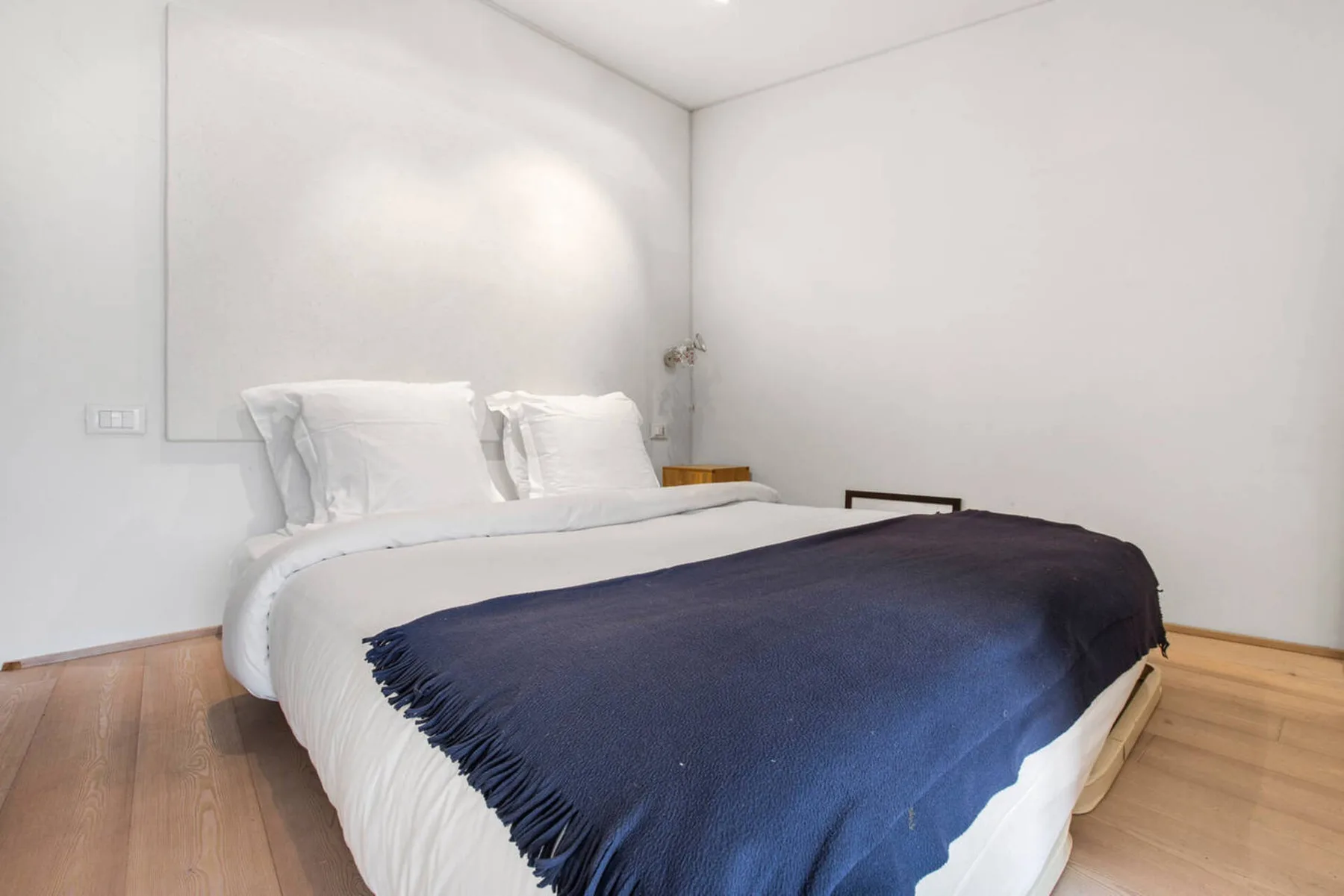 Un dormitorio con ropa de cama blanca y una manta azul oscuro.