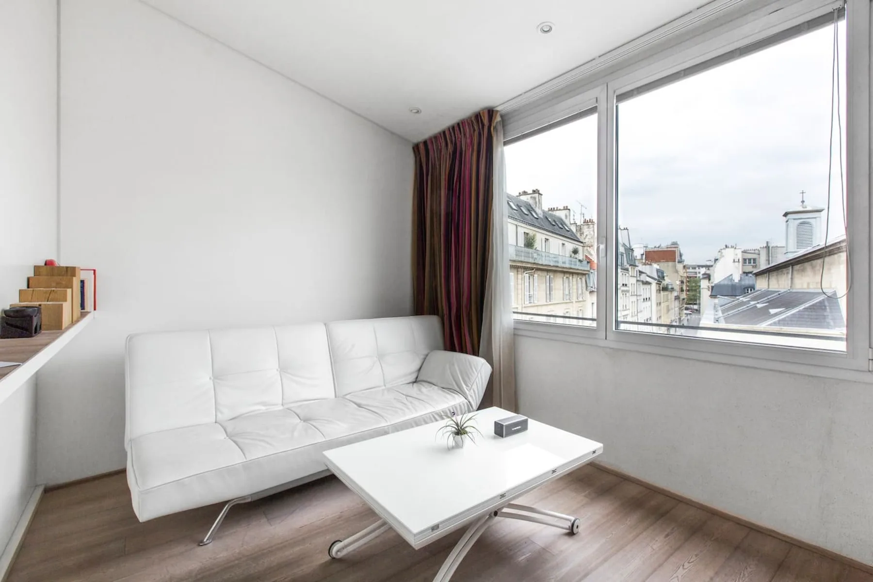 Una sala luminosa con asientos blancos junto a grandes ventanas con vistas a los tejados de la ciudad.