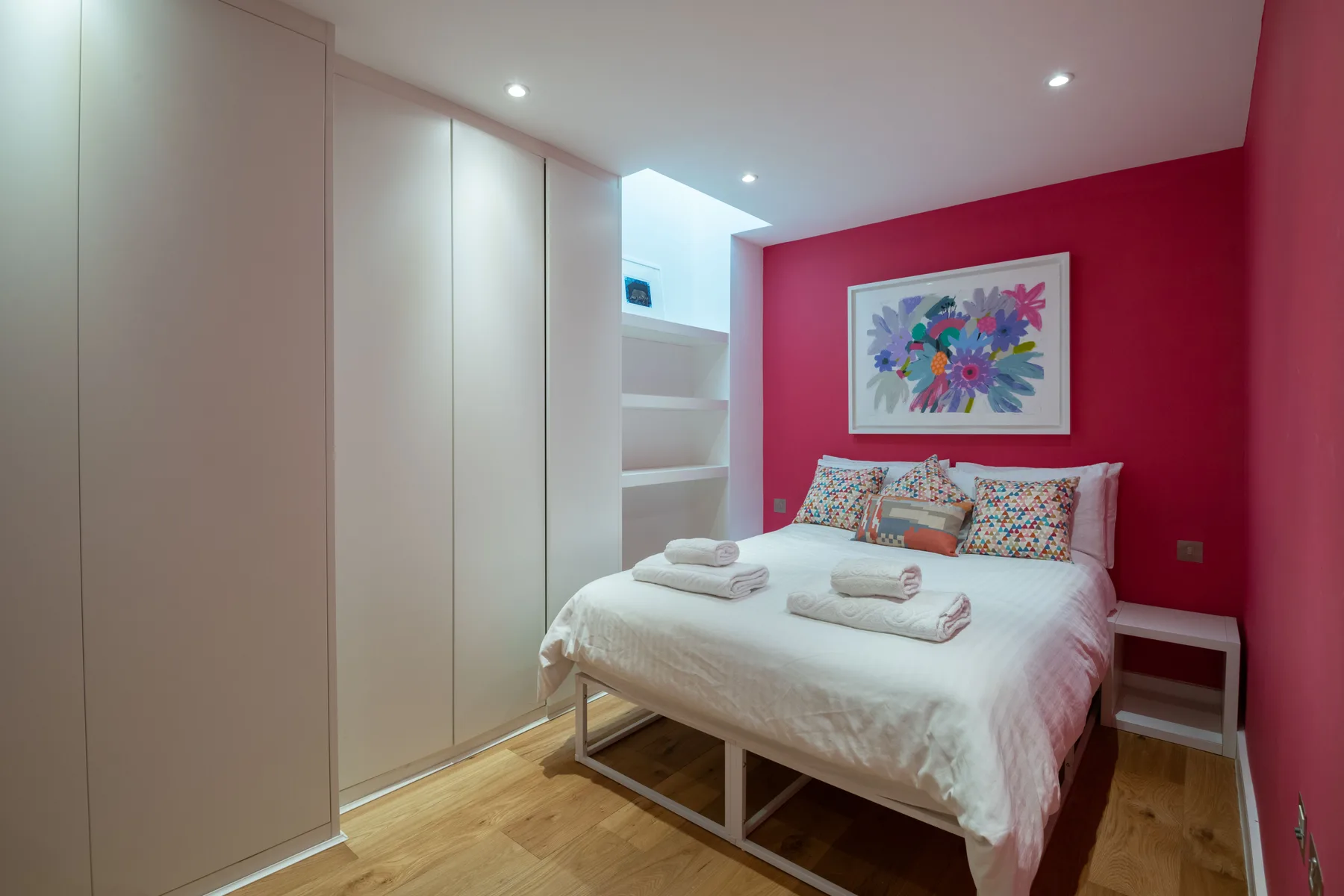 A bedroom with a neatly made bed and colorful floral artwork on the wall.