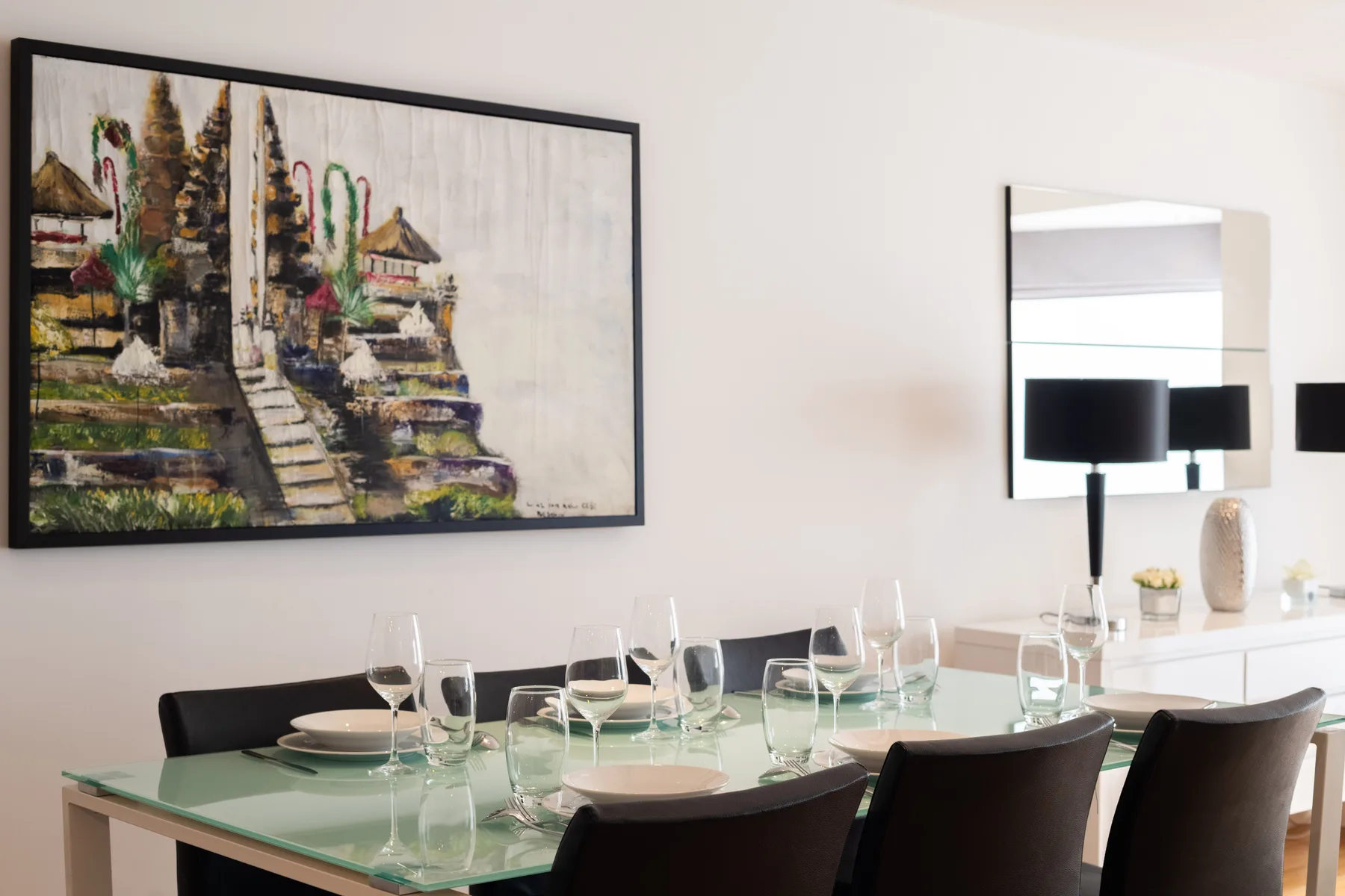 Dining area with a glass table set with plates and glassware.
